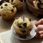Freshly baked chocolate chip muffins, golden brown with melted chocolate chips, cooling and ready to enjoy