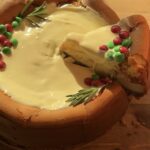 A creamy slice of Christmas cookie dough cheesecake with a cookie dough crust, filled with festive red and green M&M’s, topped with melted white chocolate and extra M&M’s for the perfect holiday treat.