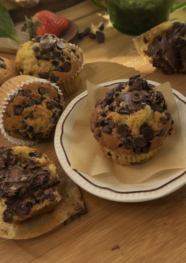 Nutella stuffed muffins on a wooden board with chocolate chips and Nutella on top.