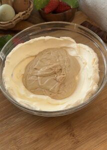 A bowl of soft cream cheese and Kinder Bueno spread ready to be mixed for the filling of a no-bake Kinder Bueno cheesecake. The creamy ingredients are smooth and inviting, promising a rich and decadent dessert.