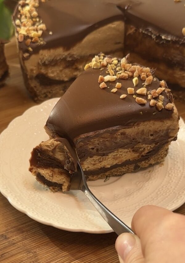 Spooning a slice of Peanut Butter Cheesecake with a perfect cookie crust, smooth peanut butter cheesecake, a rich peanut butter middle layer, and topped with Nutella and crushed peanuts, revealing the creamy inside