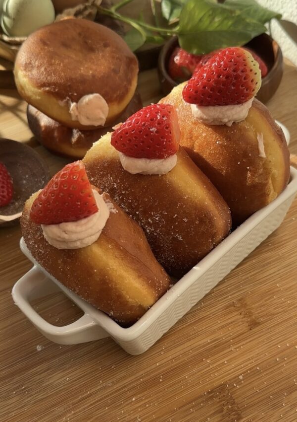 Fluffy strawberry cheesecake stuffed donuts with fresh strawberries on top, coated in sugar, showcasing their delicious filling.